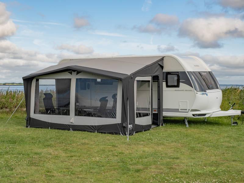 Caravan awning with mesh windows set up on grass near water, ideal for camping and outdoor adventures.