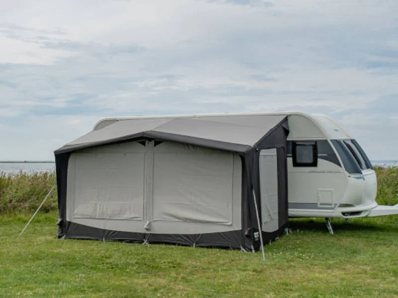 Grey caravan awning attached to white caravan on grassy field, ideal for camping and outdoor adventures.