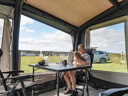Man relaxing with dog inside caravan awning, enjoying outdoor camping setup with table and chairs