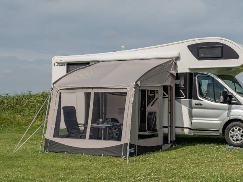 Motorhome awning with mesh windows and outdoor furniture on grassy field