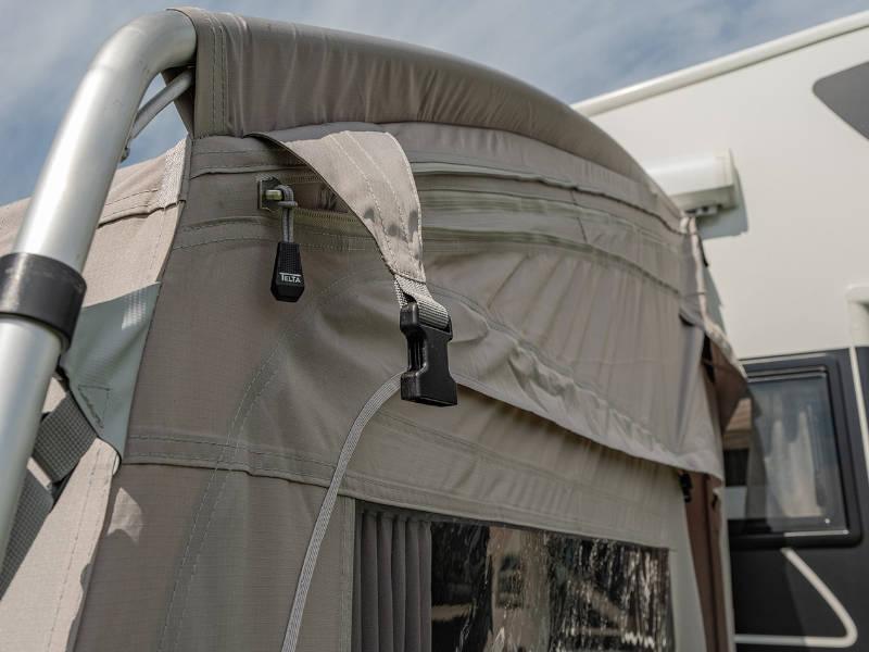 Beige caravan awning with zippered window and adjustable straps, attached to motorhome for outdoor camping.