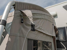 Beige caravan awning with zippered window and adjustable straps, attached to motorhome for outdoor camping.