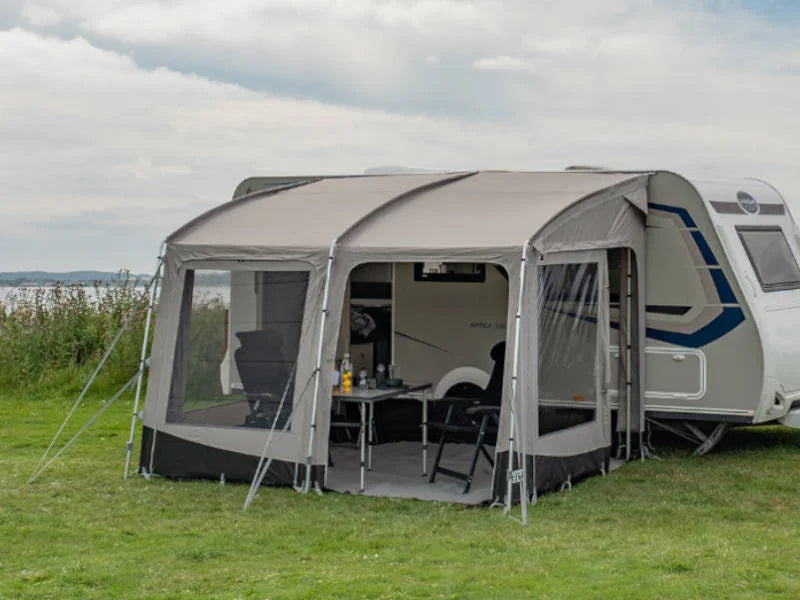 Caravan awning with mesh windows set up on grass, featuring outdoor table and chairs for camping adventures.