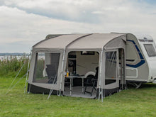 Caravan awning with mesh windows set up on grass, featuring outdoor table and chairs for camping adventures.