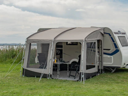 Caravan awning with mesh windows set up on grass, featuring outdoor table and chairs for camping adventures.