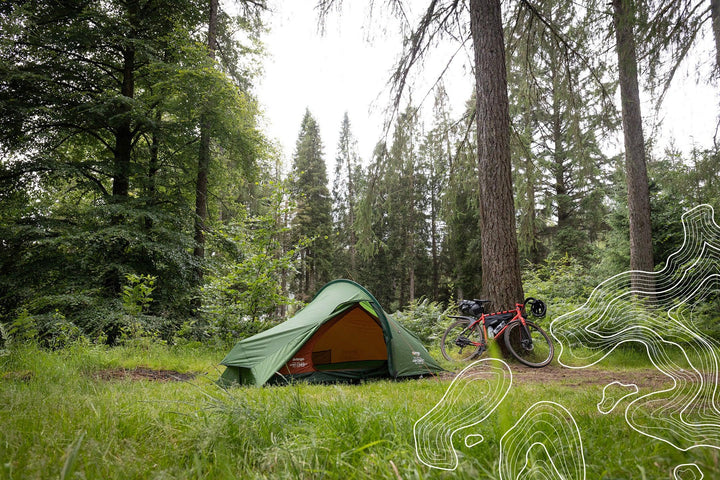 Green camping tent in forest with red bike, ideal for outdoor adventures and camping gear