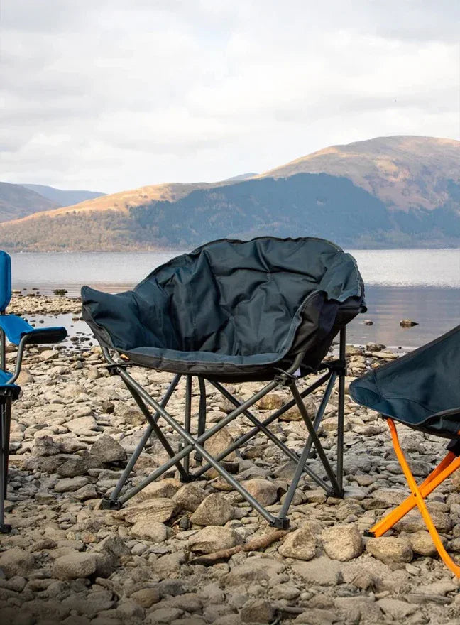 Folding chairs on a rocky shore with a scenic mountain and lake background