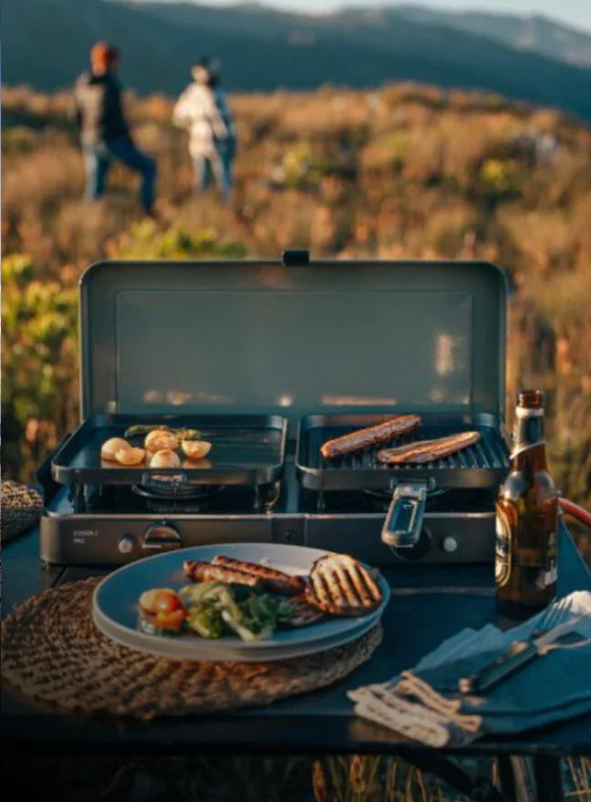 Portable grill with food on a table outdoors, people in the background
