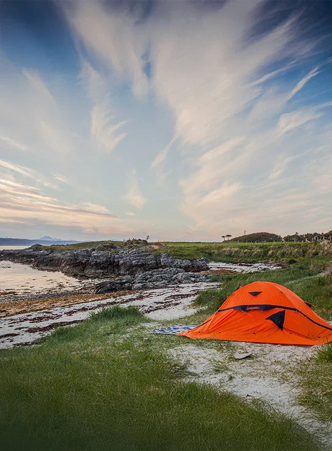 Orange tent pitched on a grassy area near a coastal landscape with a dramatic sky.