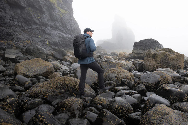 Hiker with backpack navigating rocky coastal terrain, ideal for outdoor adventure gear and camping equipment.