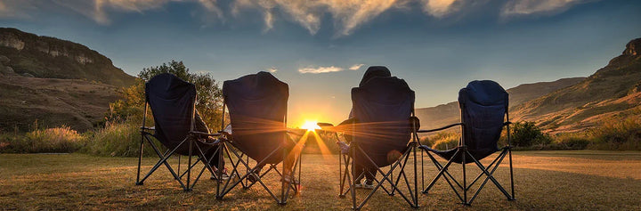 Four people relaxing in camping chairs at sunset, enjoying outdoor adventure with scenic mountain views.