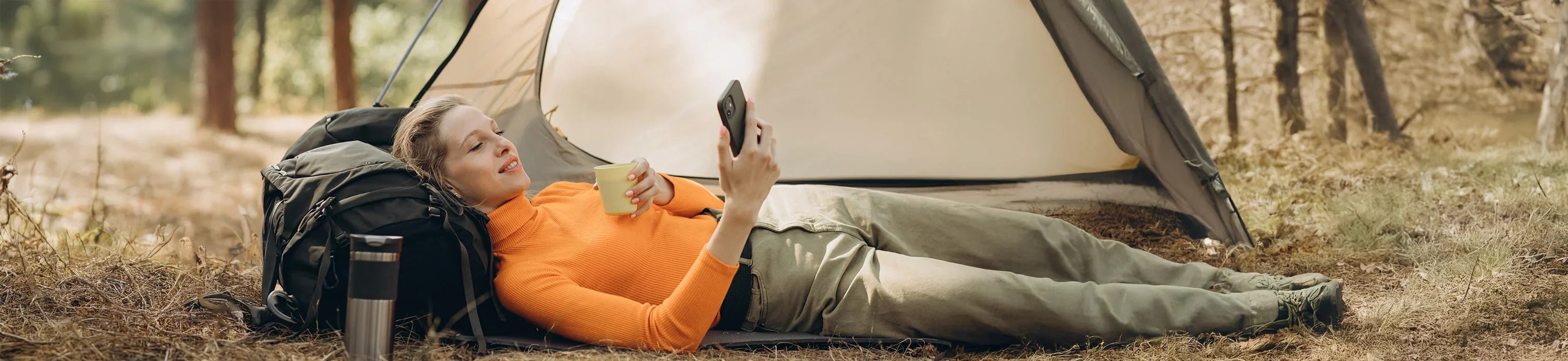 Woman relaxing outdoors with camping tent, backpack, and coffee mug, enjoying nature on camping trip