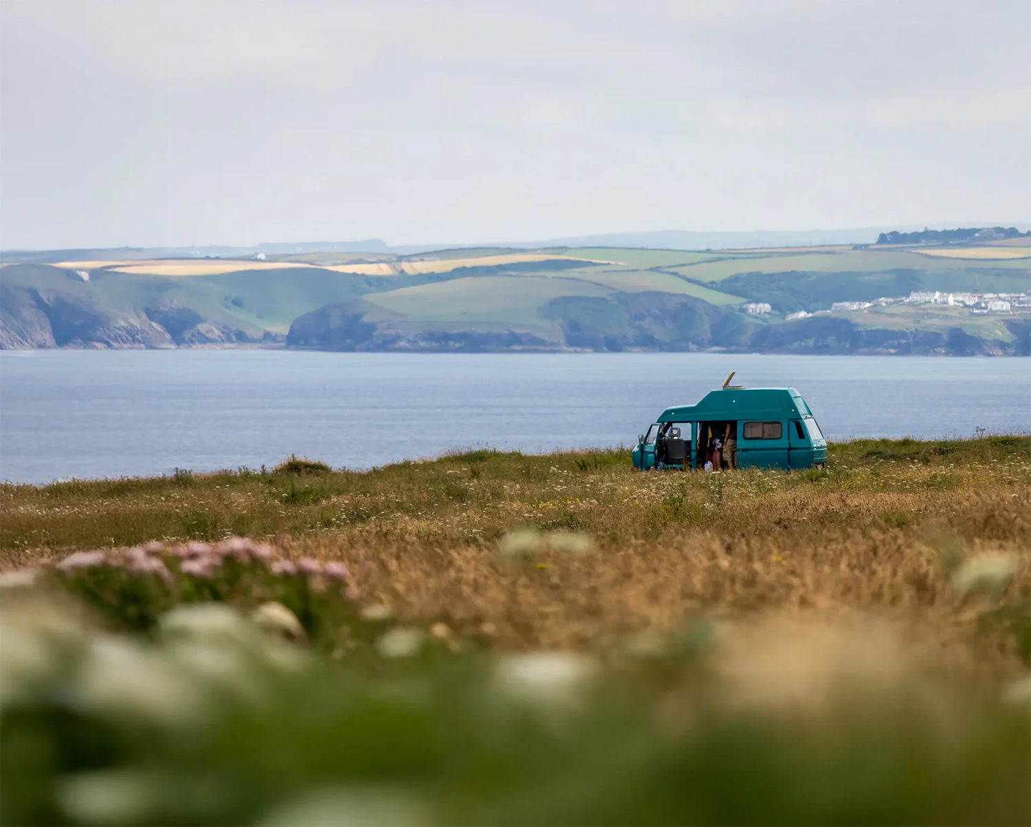 Teal campervan parked on coastal cliff overlooking sea, perfect for caravanning adventures and outdoor escapes.