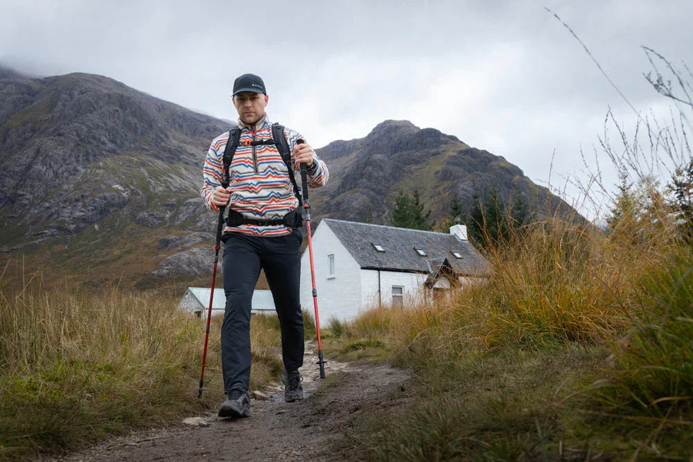 Man hiking with trekking poles on mountain trail near cottage, wearing outdoor gear for adventure