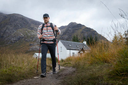 Man hiking with trekking poles on mountain trail near cottage, wearing outdoor gear for adventure