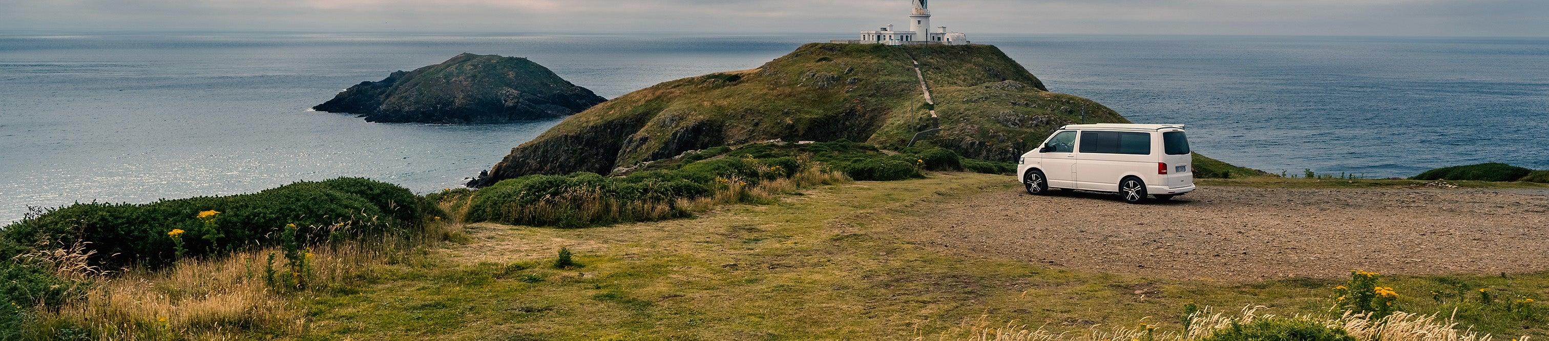 White campervan parked on coastal cliff near lighthouse, ideal for motorhome adventures and outdoor travel