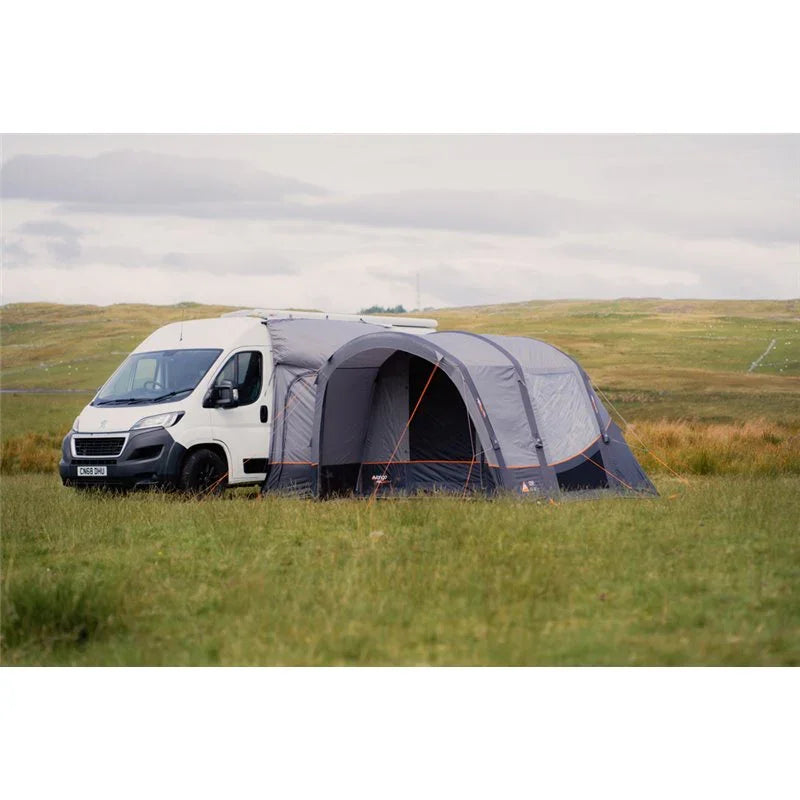Motorhome awning attached to white van in grassy field for outdoor camping adventures