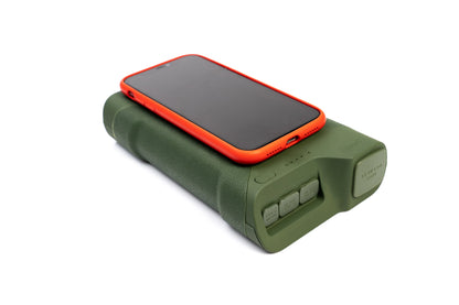 Green portable power bank charging red phone, ideal for camping and outdoor adventures with USB and 12V outputs.